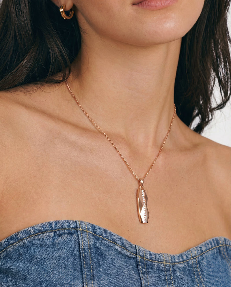 Gold-plated faceted bar pendant necklace with a vertical pavé strip, worn at the collarbone with a denim neckline.