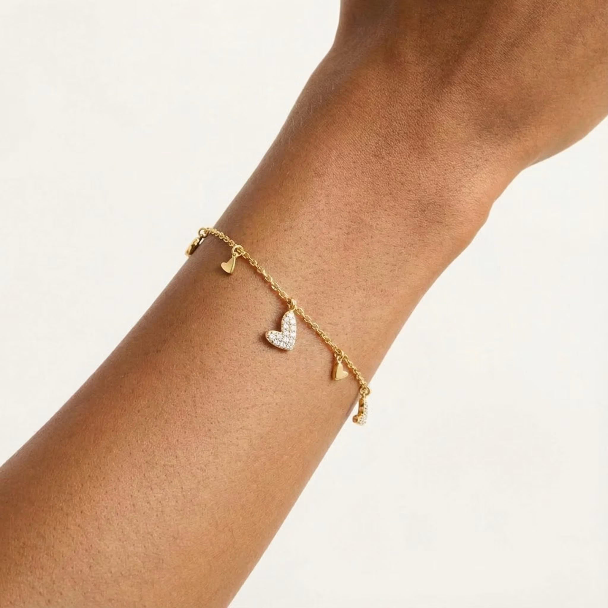 Gold-plated charm bracelet with a pavé heart centerpiece worn on the wrist.