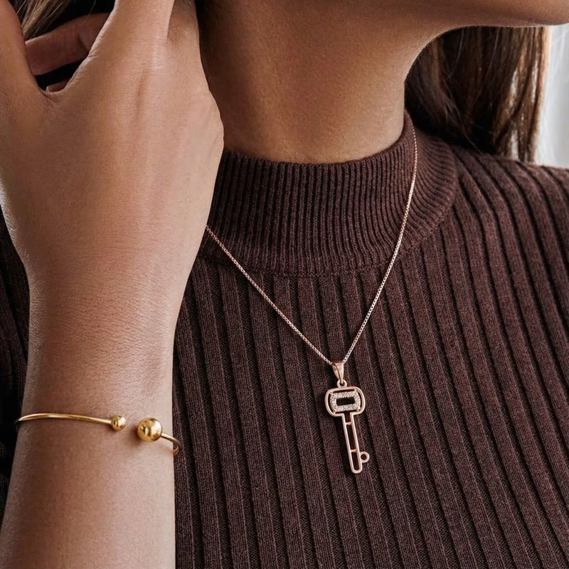 Gold-plated key pendant necklace with CZ accents, worn on the neck over a brown ribbed top.