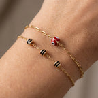 Gold-plated bracelet with black and red beads on a wrist against a neutral background
