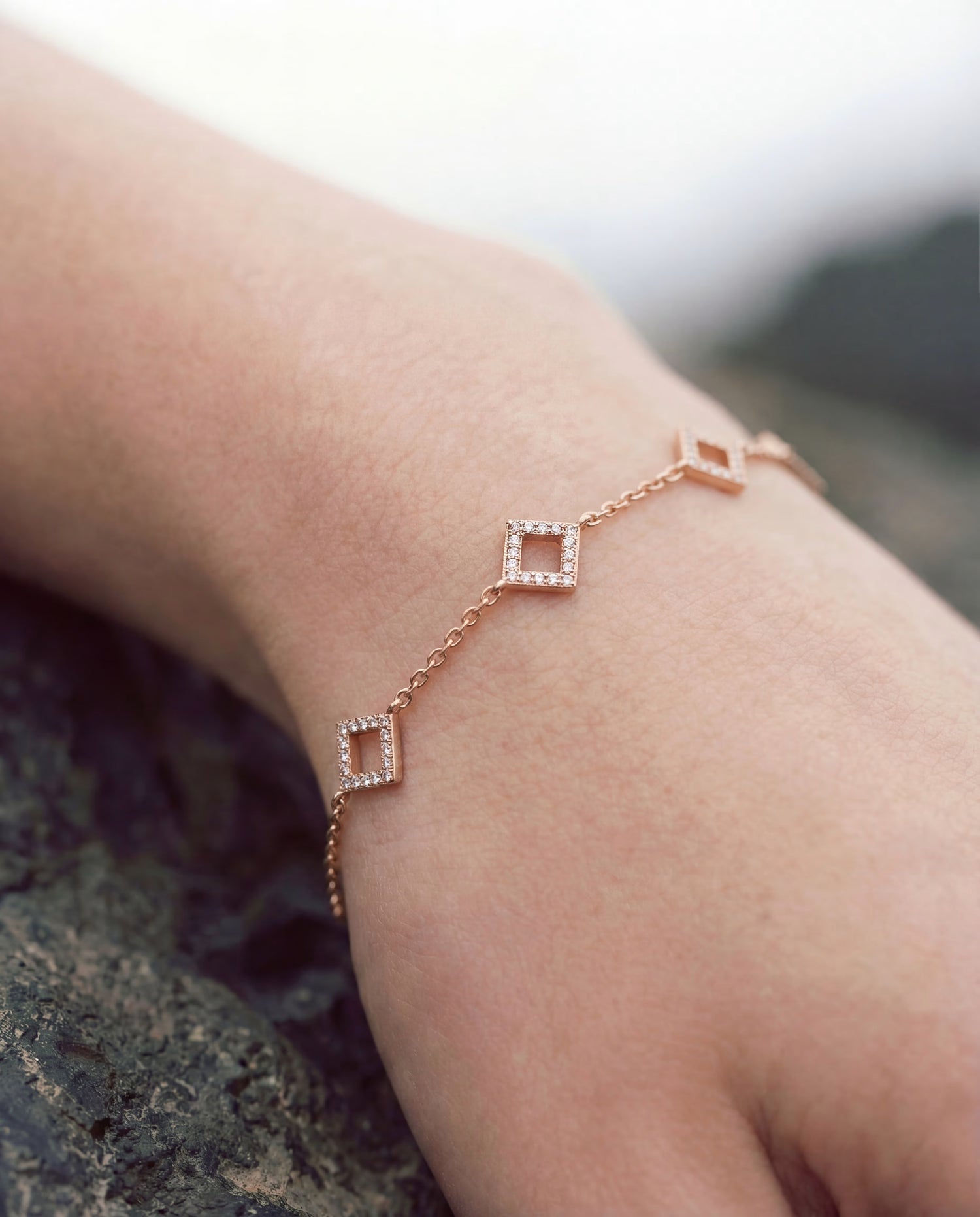 Gold-plated chain bracelet with open square links outlined in pavé stones, photographed close-up on the wrist.